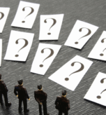 Miniature business figures standing before multiple question cards, representing decision-making