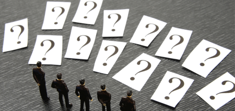 Miniature business figures standing before multiple question cards, representing decision-making