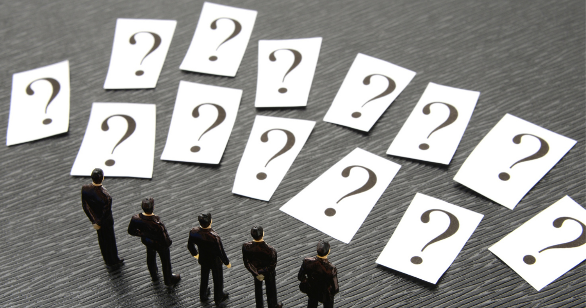 Miniature business figures standing before multiple question cards, representing decision-making