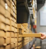 Person retrieving a product box from warehouse shelving using inventory accounting software to track stock levels