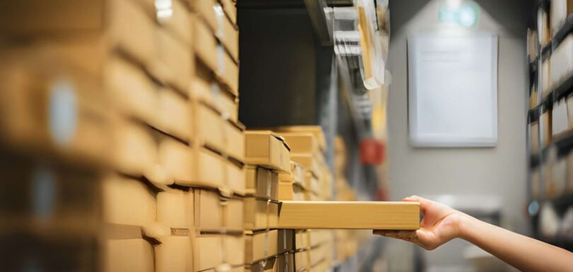 Person retrieving a product box from warehouse shelving using inventory accounting software to track stock levels